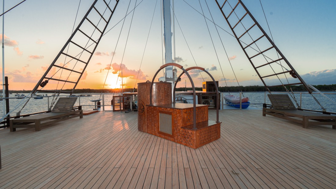 An Ikigai teak ice bath on the deck of a wooden boat at sunset